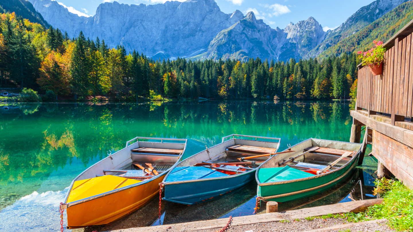 Three colourful rowboats on a emerald lake in Italy with mountains in the background.